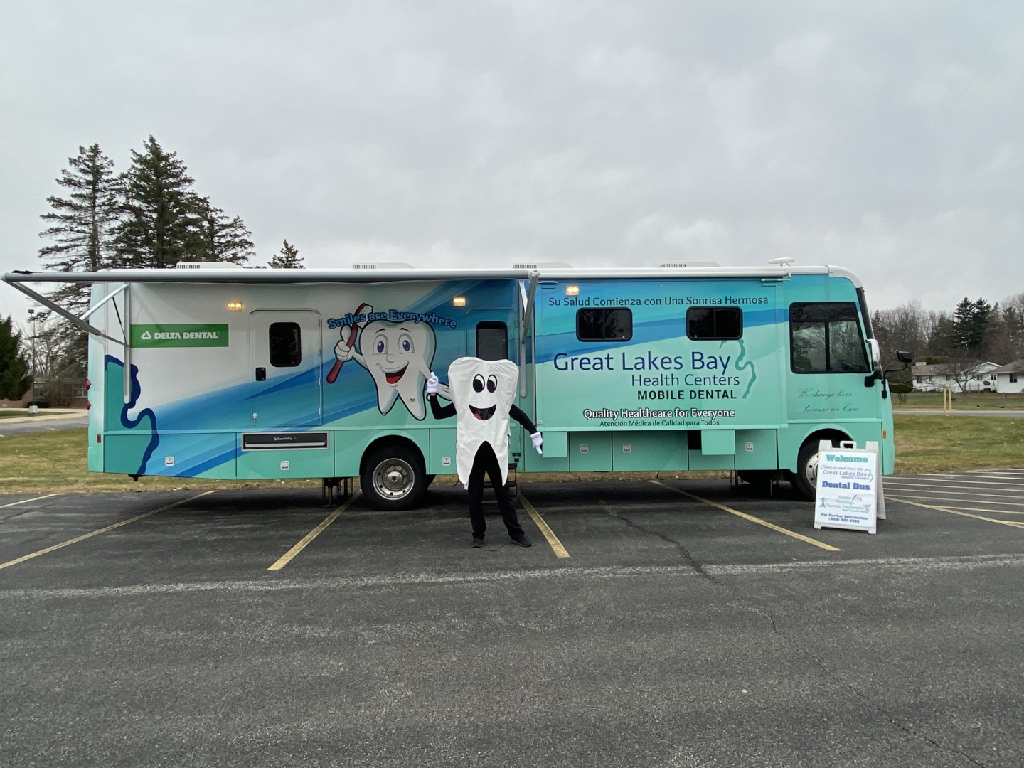 Pop up mobile dental clinic with tooth mascot standing in front of bus